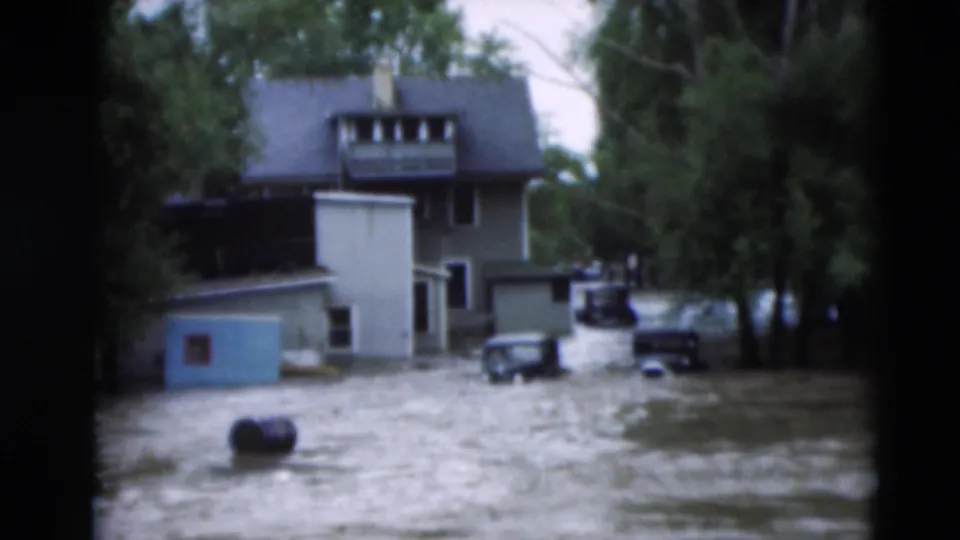 Paducah, Kentucky flood footage from 1951 showing muddy water around homes, trees, parked cars, and a blue shed.