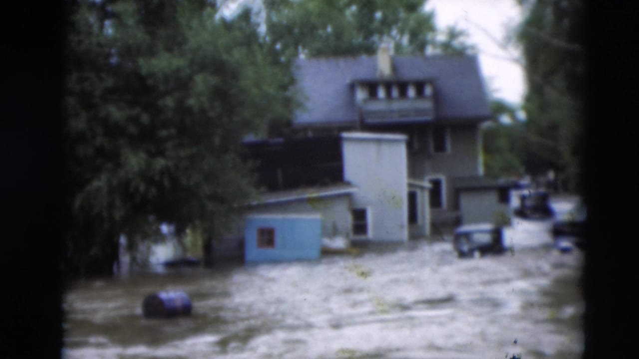 1951 Paducah flood scene with standing water around a two-story home, a blue shed, trees, and older vehicles.
