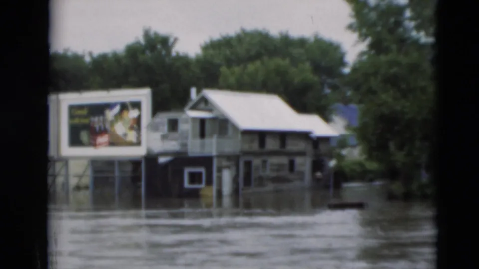 1951 Paducah flood scene with water around a small building, roadside billboard, trees, and adjacent structures.