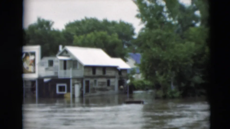 Paducah floodwater surrounds residential buildings, trees, and a partially readable billboard in this 1951 8mm frame.