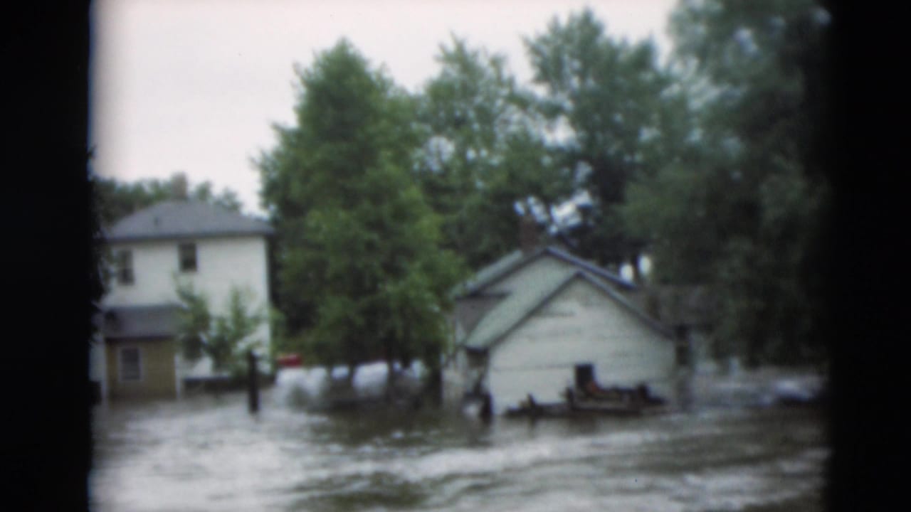 1951 Paducah, Kentucky 8mm frame showing muddy floodwater around a small house, trees, and nearby residential structures.