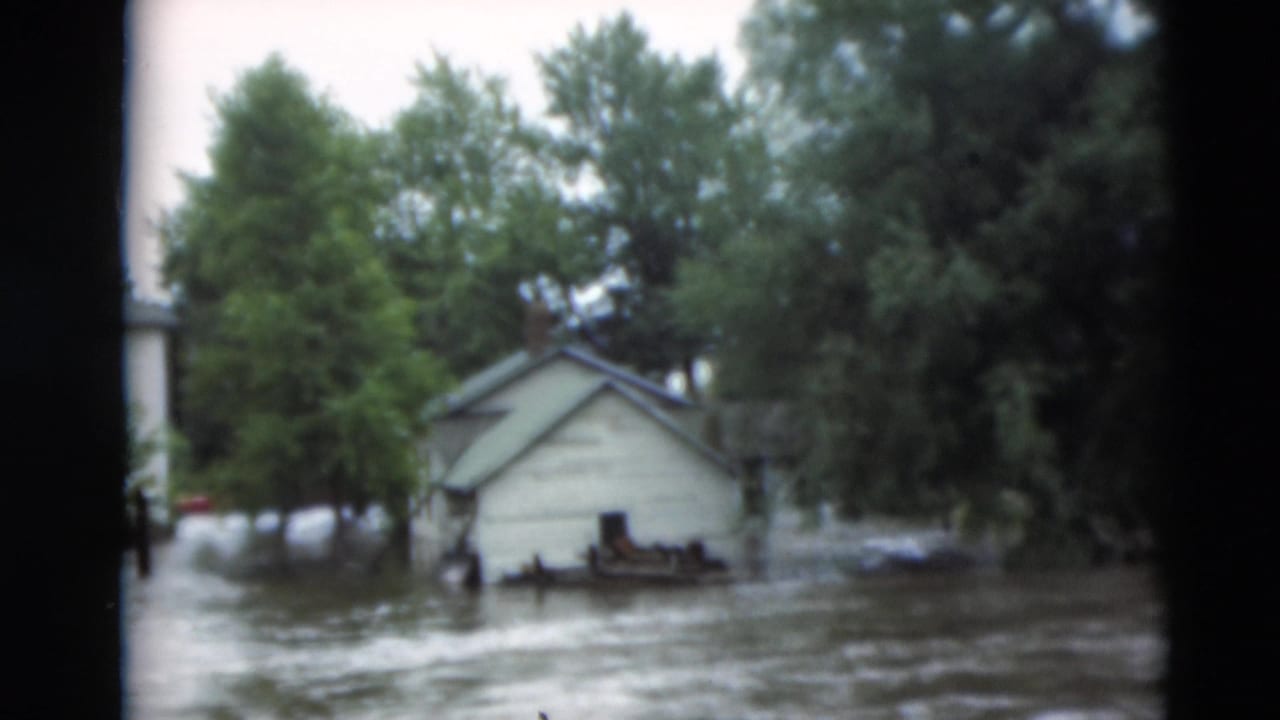 A small outbuilding stands in high muddy water with trees behind it.