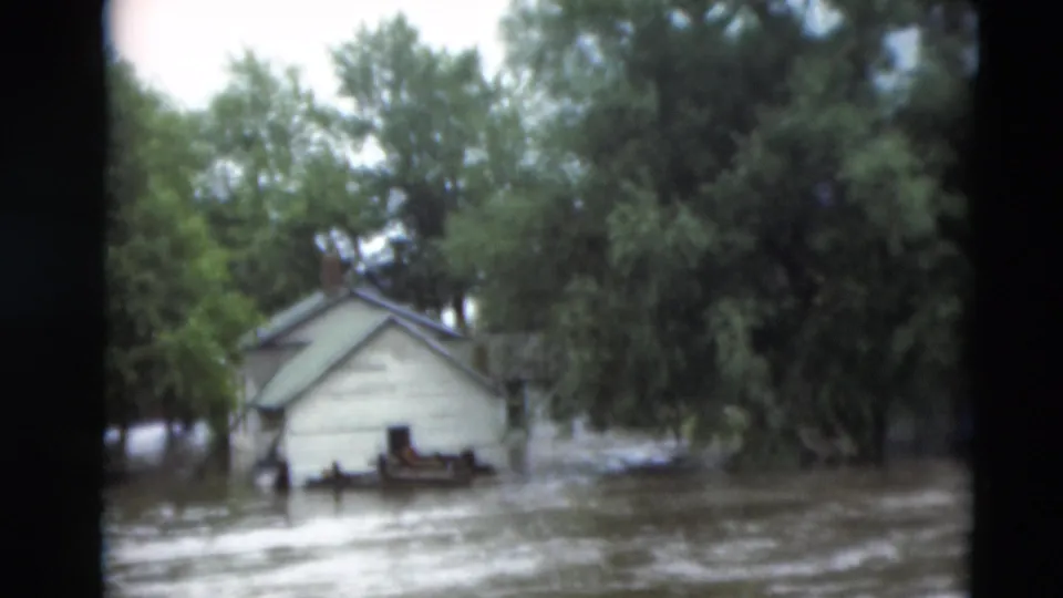 1951 Paducah, Kentucky 8mm frame showing muddy water flowing past a small building, trees, and partially submerged yard features.