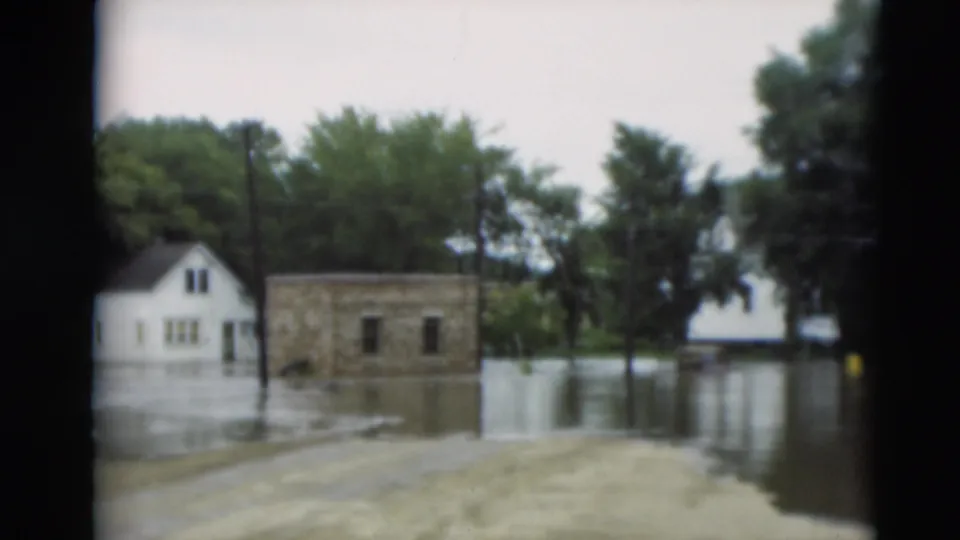 1951 Paducah, Kentucky home-movie frame with a white house, small building, trees, and utility poles surrounded by floodwater.