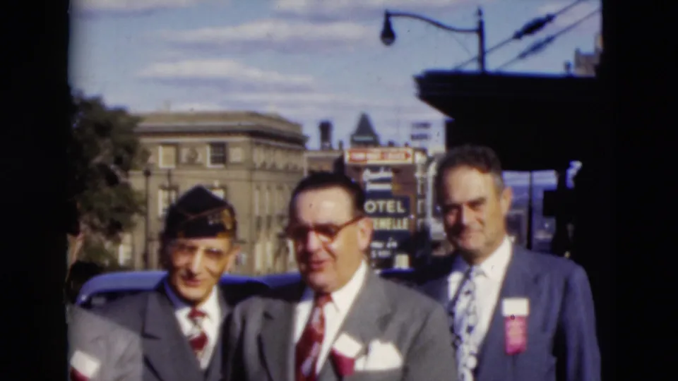 Three older men in formal suits face the camera in Paducah, with a shaded overhang, parked cars, and mid-century buildings behind them.