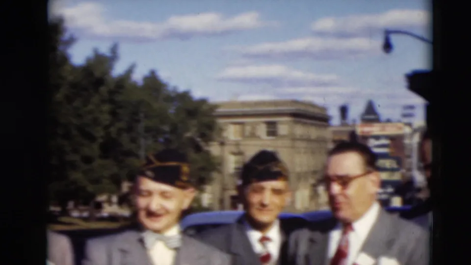 Three suited men, including two in dark caps, stand on a Paducah street in 1951 while a partially visible person appears at the left edge.