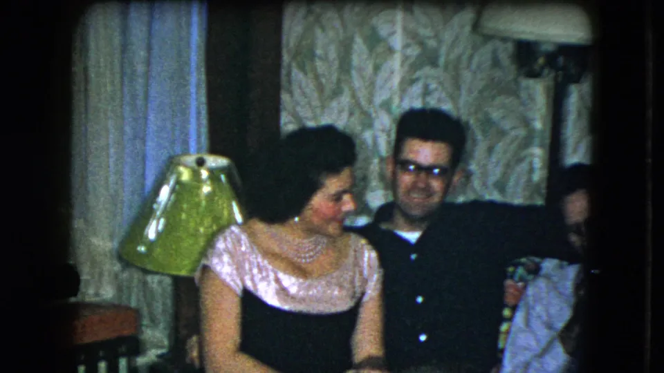 1951 Cleveland home-movie frame showing adults seated close together during a relaxed indoor celebration.