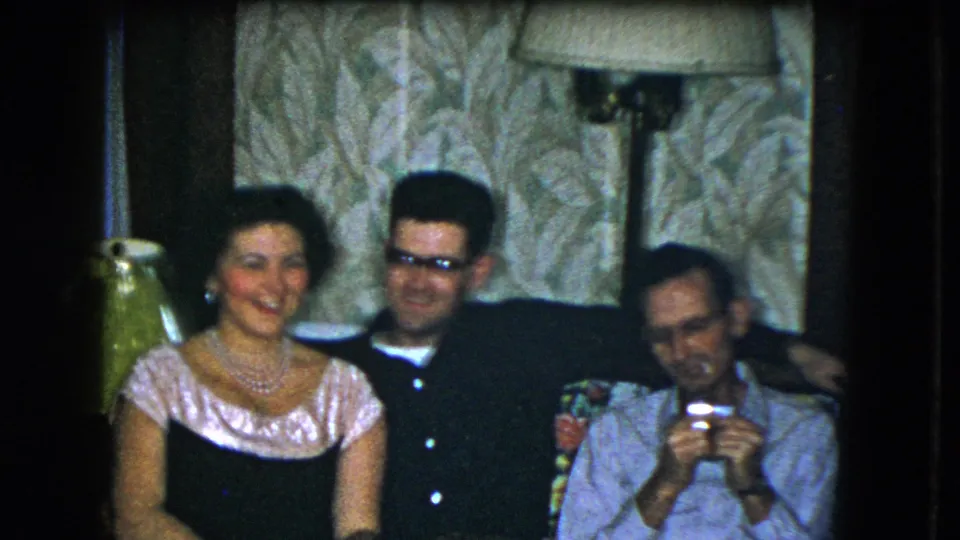 1951 Cleveland home-movie frame of three adults seated together, smiling and relaxing in a private living room.