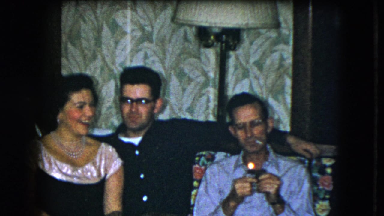 In 1951 Cleveland home-movie footage, a woman and two men sit together on a floral couch beneath leafy wallpaper and a lamp.