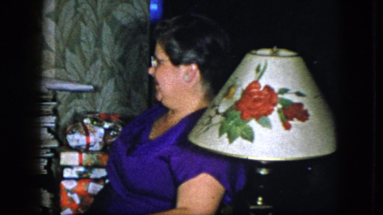 The woman turns in profile beside a floral lampshade, patterned wallpaper, magazines, and wrapped gifts in the Cleveland interior.