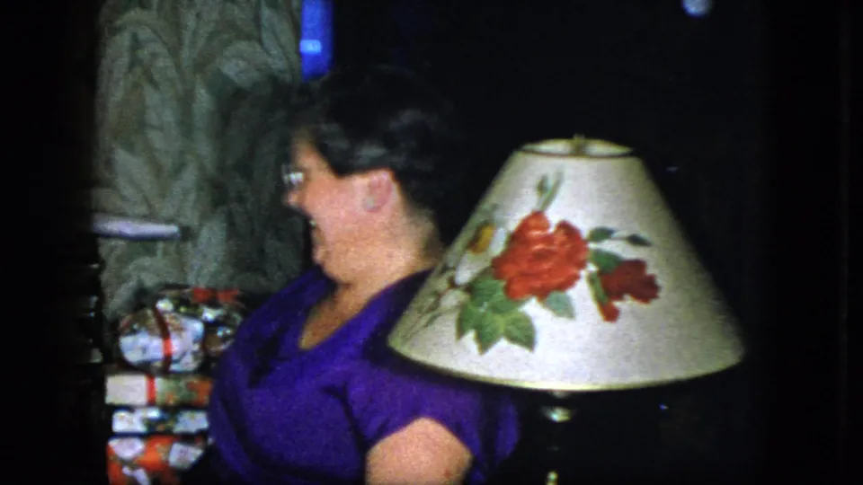 The woman laughs while seated near a floral lampshade, with wrapped gifts and patterned wallpaper visible in the 1951 home interior.