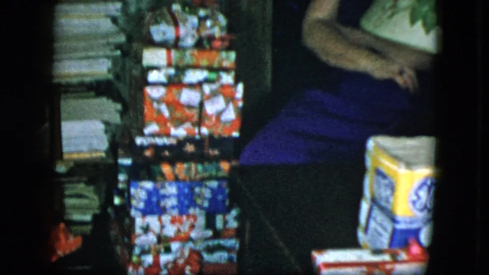 1951 Cleveland home interior showing stacked Christmas gifts, a seated woman, papers at left, and a yellow GE-branded box.