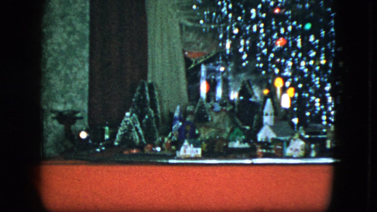 1951 Cleveland 8mm frame showing a tabletop Christmas village, artificial trees, a small rocket-like ornament, and tinsel-lit tree above a red base.