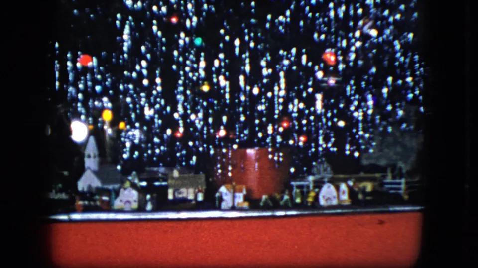1951 Cleveland frame with a wider view of the model train, small village buildings, fence pieces, tinsel, and colored Christmas lights above a red base.