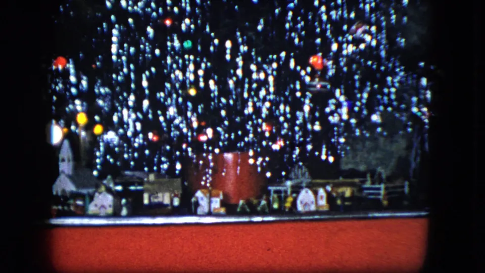 1951 Cleveland home-movie frame showing a tinsel-covered Christmas tree over small houses, ornaments, and a train display.