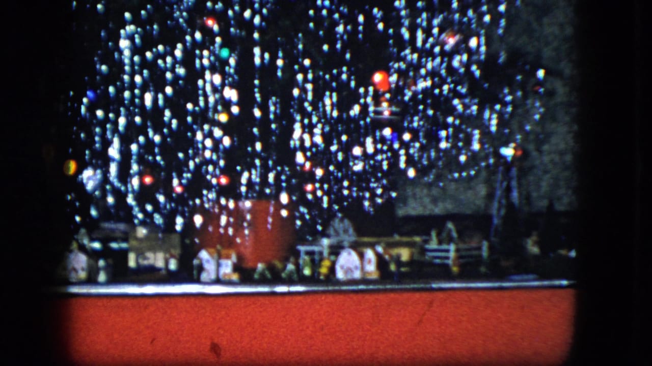 1951 Cleveland frame of a decorated Christmas tree, small village pieces, train track, and red floor covering.