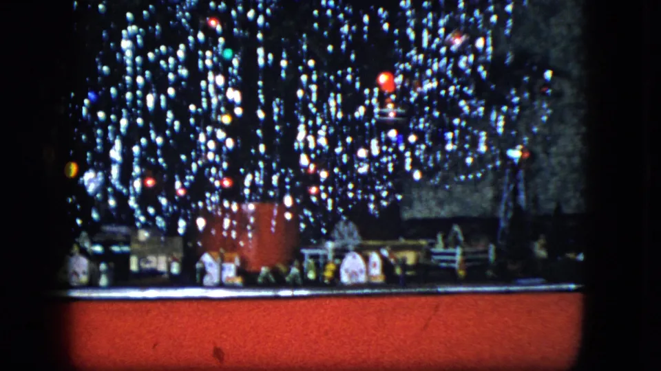1951 Cleveland frame of a decorated Christmas tree, small village pieces, train track, and red floor covering.