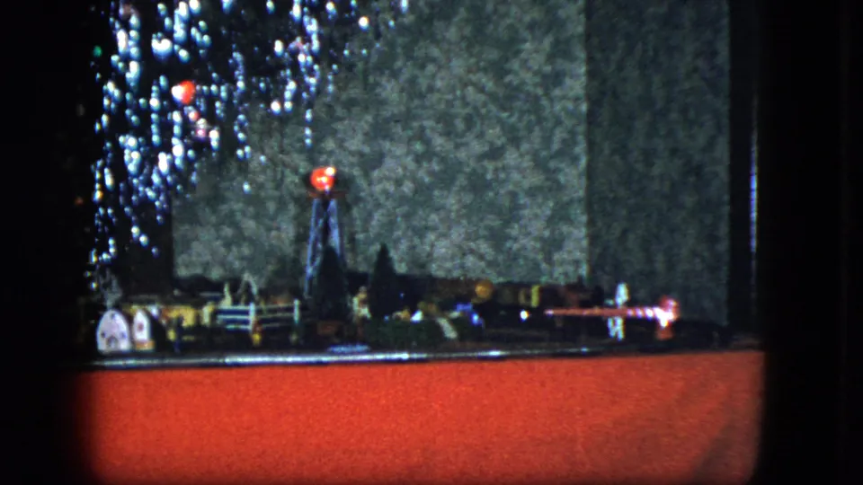 Side-angle 8mm frame of a Cleveland holiday model train scene with small buildings and bright tree lights.