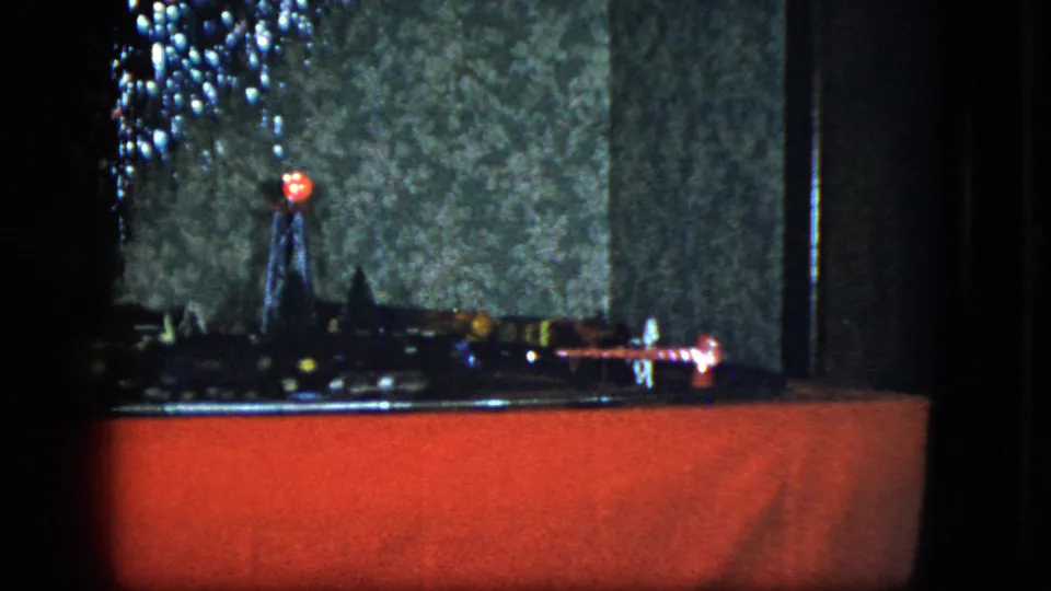 Cleveland 1951 8mm frame of a model train display crossing a red platform beneath Christmas tree lights.