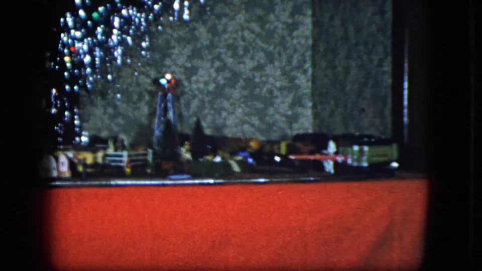 1951 Cleveland home-movie frame with a miniature town and train layout under a Christmas tree, seen from a fixed low angle.