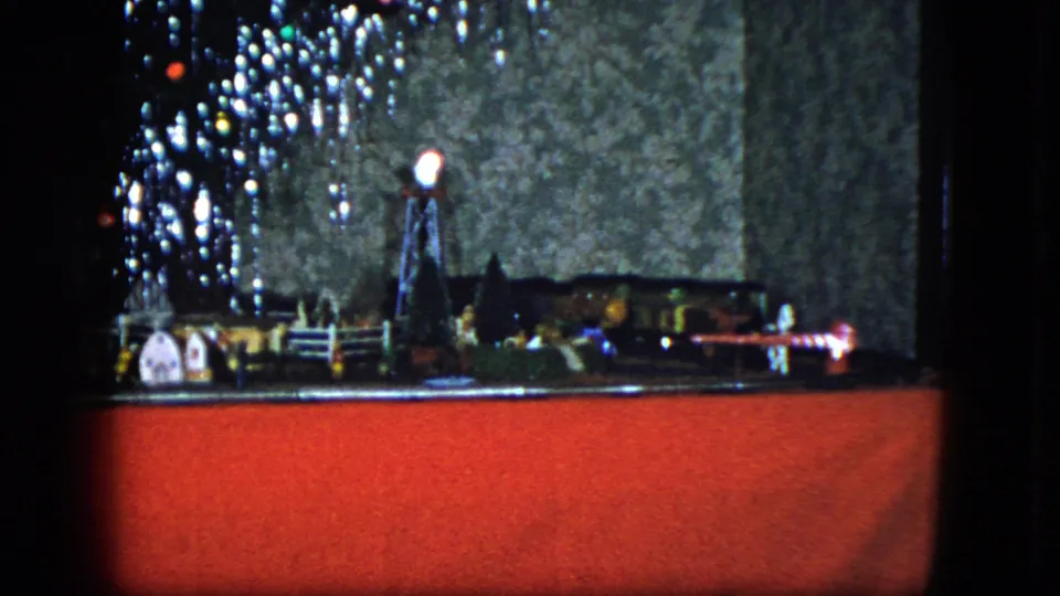 1951 Cleveland home-movie frame showing a toy train display with miniature buildings, tree lights, and a windmill-like piece.