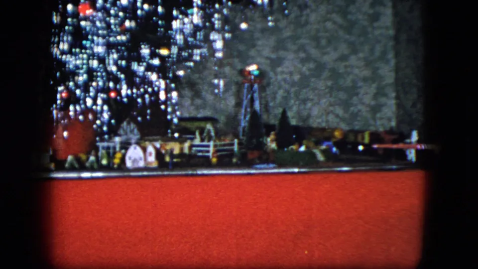 1951 Cleveland home-movie frame with bright Christmas tree lights over a miniature train town and red floor covering.