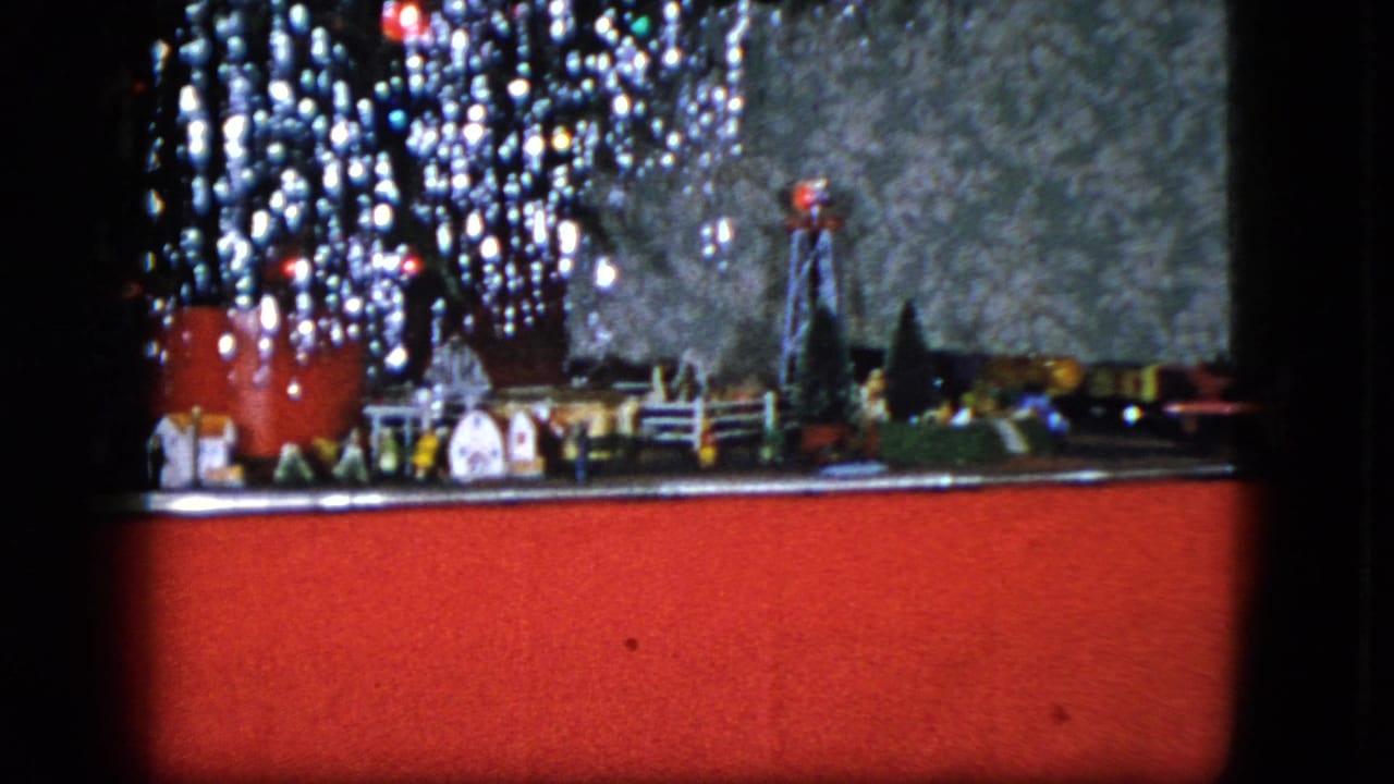 Miniature Christmas display with a toy railroad track, small buildings, tinsel, and a red base panel.