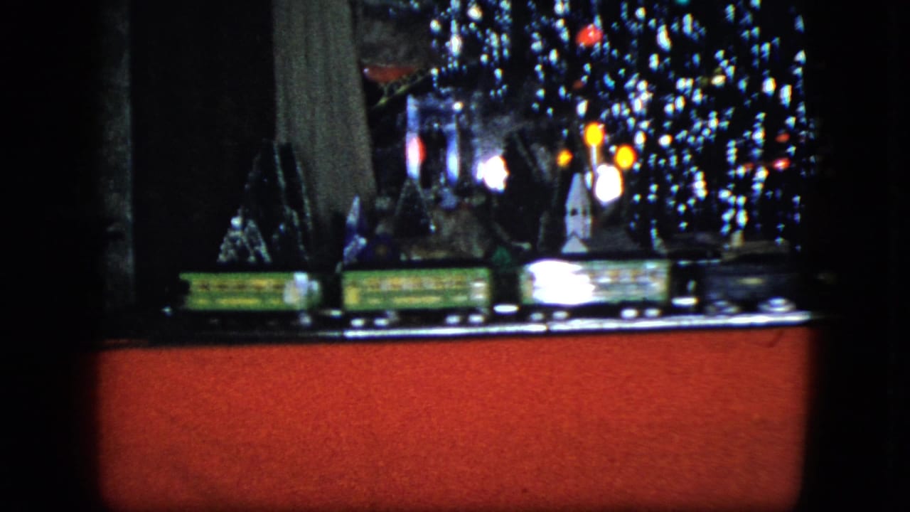 Toy train display with tinsel, small model buildings, lights, and a red base panel.