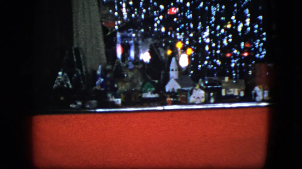 1951 Cleveland frame of a miniature Christmas village featuring a small church-like building, clustered houses, reflective tinsel, and a red display base.