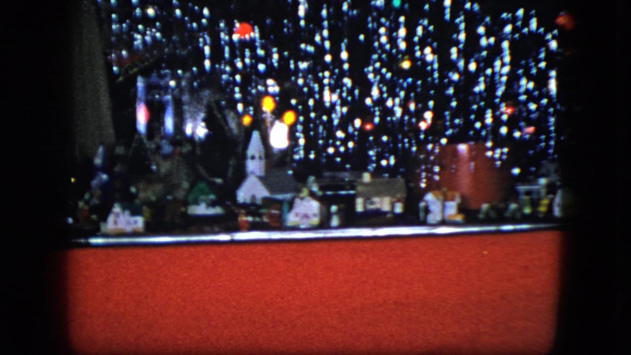 Miniature Christmas village with a church, houses, train car, and bright lights behind a red foreground edge.
