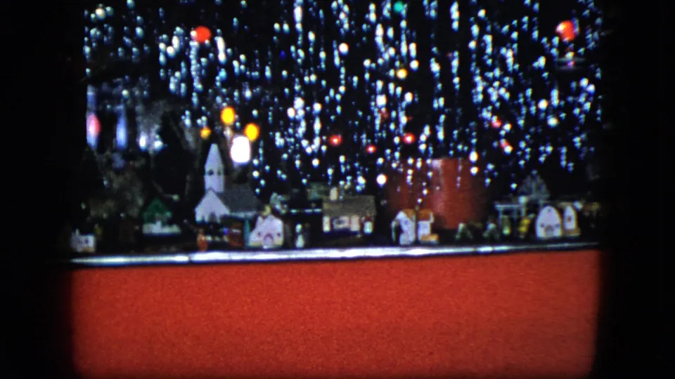 1951 Cleveland home-movie frame of a Christmas model train setup with a miniature church, houses, red train car, and lights.