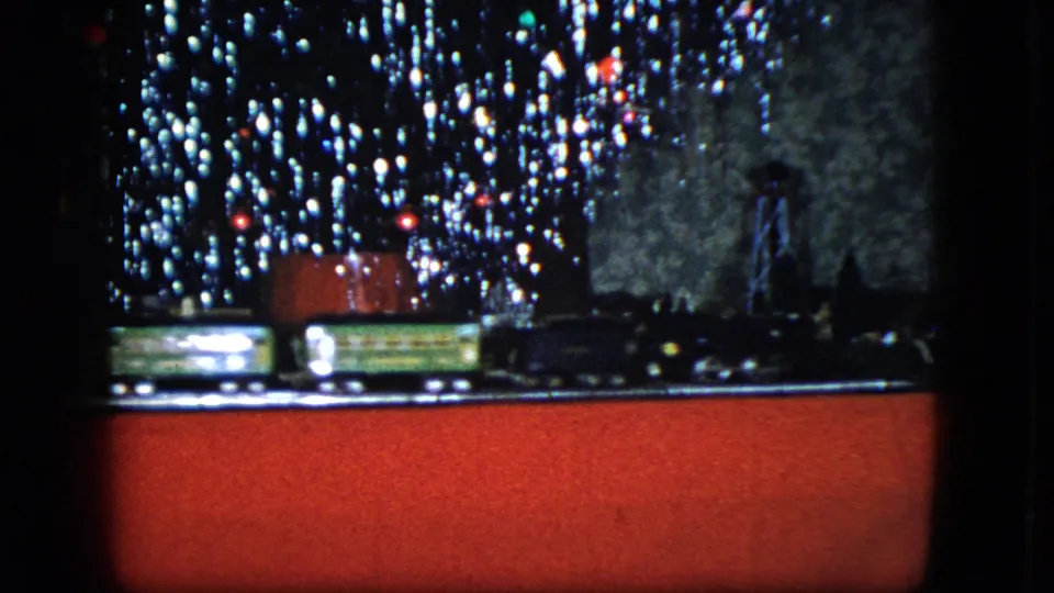 A Cleveland 1951 holiday home movie frame shows train cars moving through a miniature setup under tree lights.
