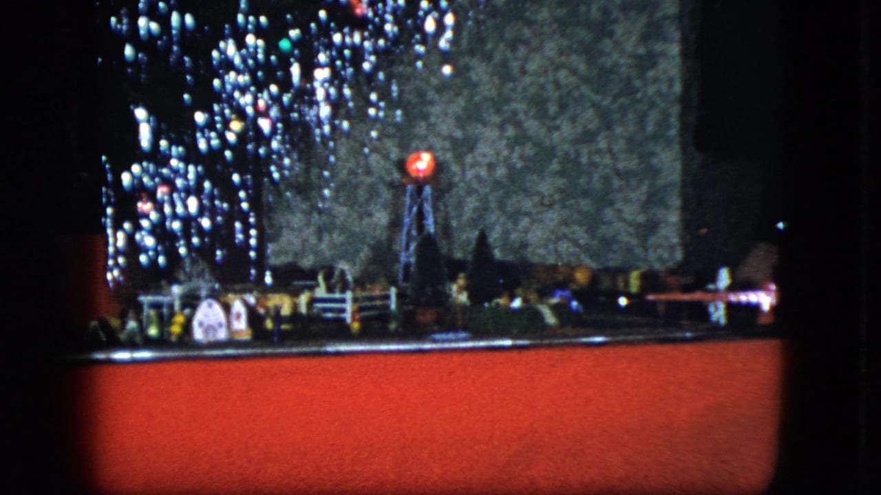 1951 Cleveland footage frame with a holiday train layout, glowing signal, miniature structures, tree lights, and a hand near the right side.