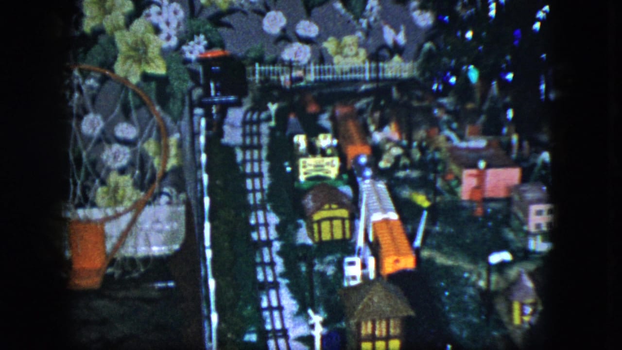 1951 Cleveland frame of a detailed indoor model train layout with small buildings, track sections, and decorative wallpaper in the background.