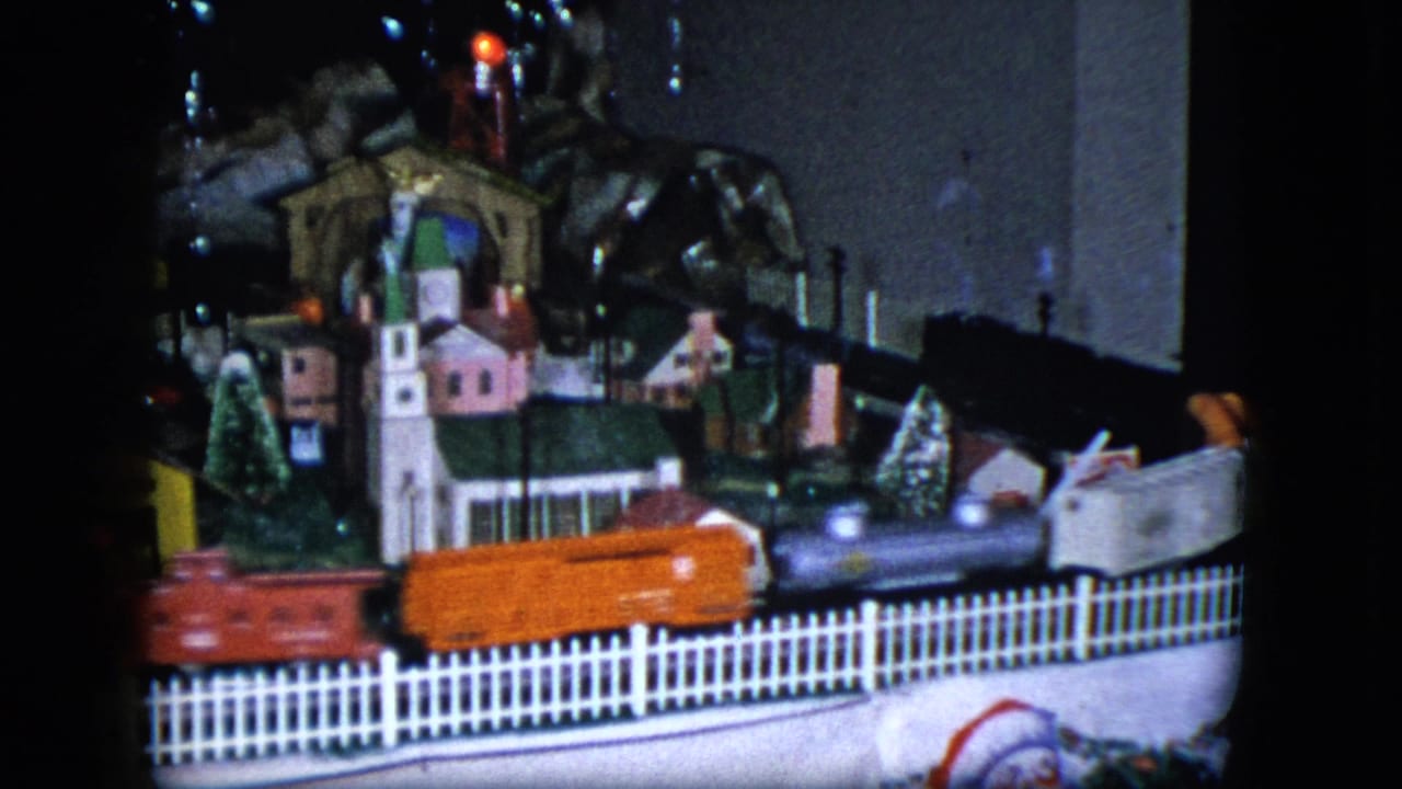 1951 Cleveland home-movie frame showing a toy train moving past a miniature church, houses, trees, and a white picket fence.