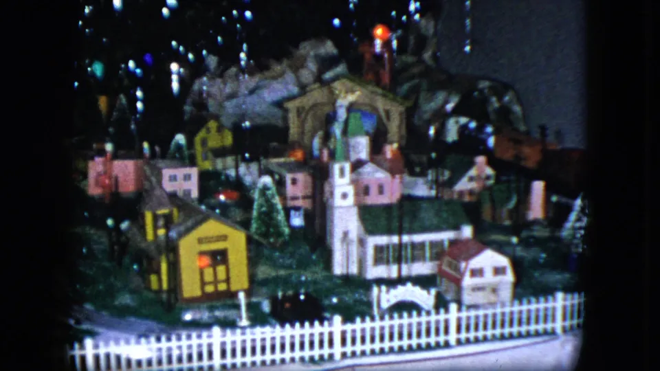 1951 Cleveland 8mm frame showing the toy village from a lower angle, with a church, yellow building, houses, fence, and lights.