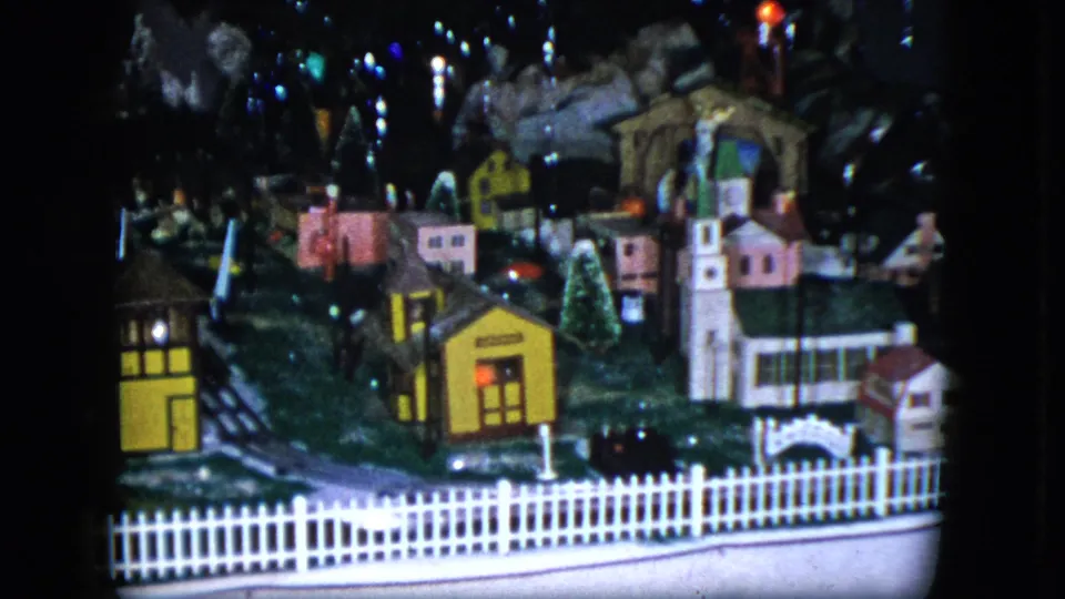 1951 Cleveland home-movie frame showing the miniature village, church, white fence, track area, and small buildings in a holiday display.