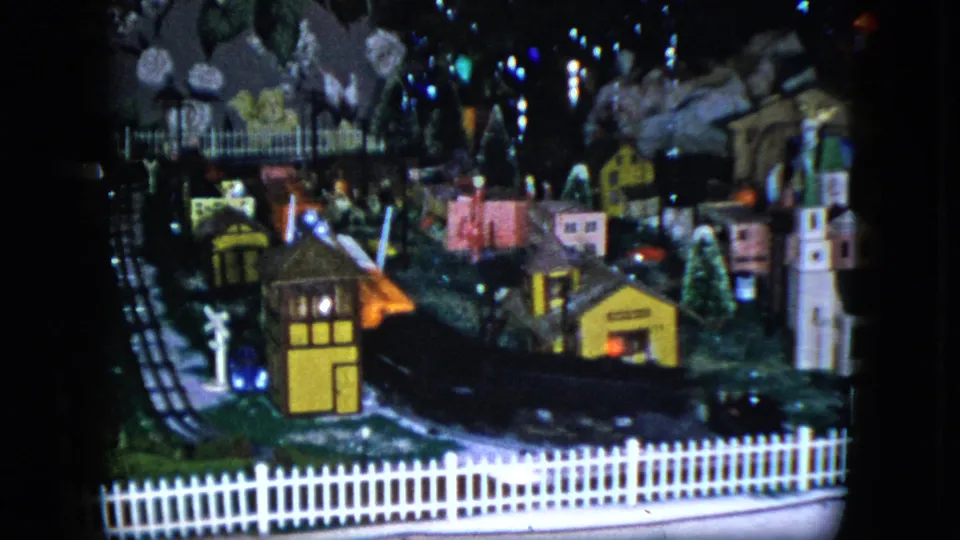 1951 Cleveland 8mm frame showing a dark toy train moving past miniature houses and landscaped tracks.