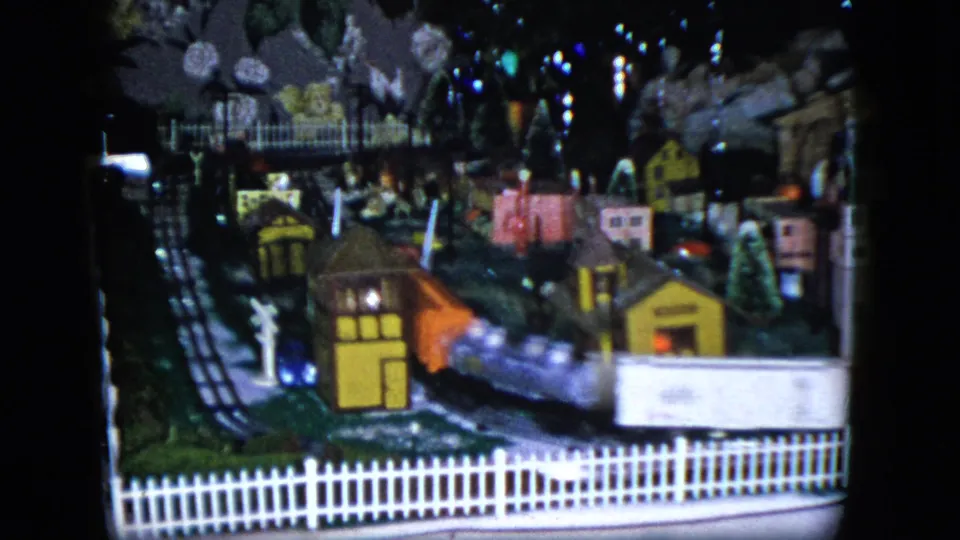 1951 Cleveland home-movie frame with a white model train car crossing the foreground of a miniature village display.