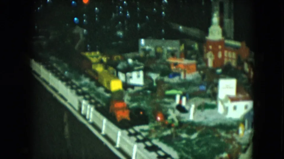 1951 Cleveland 8mm frame of a model railroad scene with tracks, clustered miniature buildings, colored bulbs, and a church steeple.