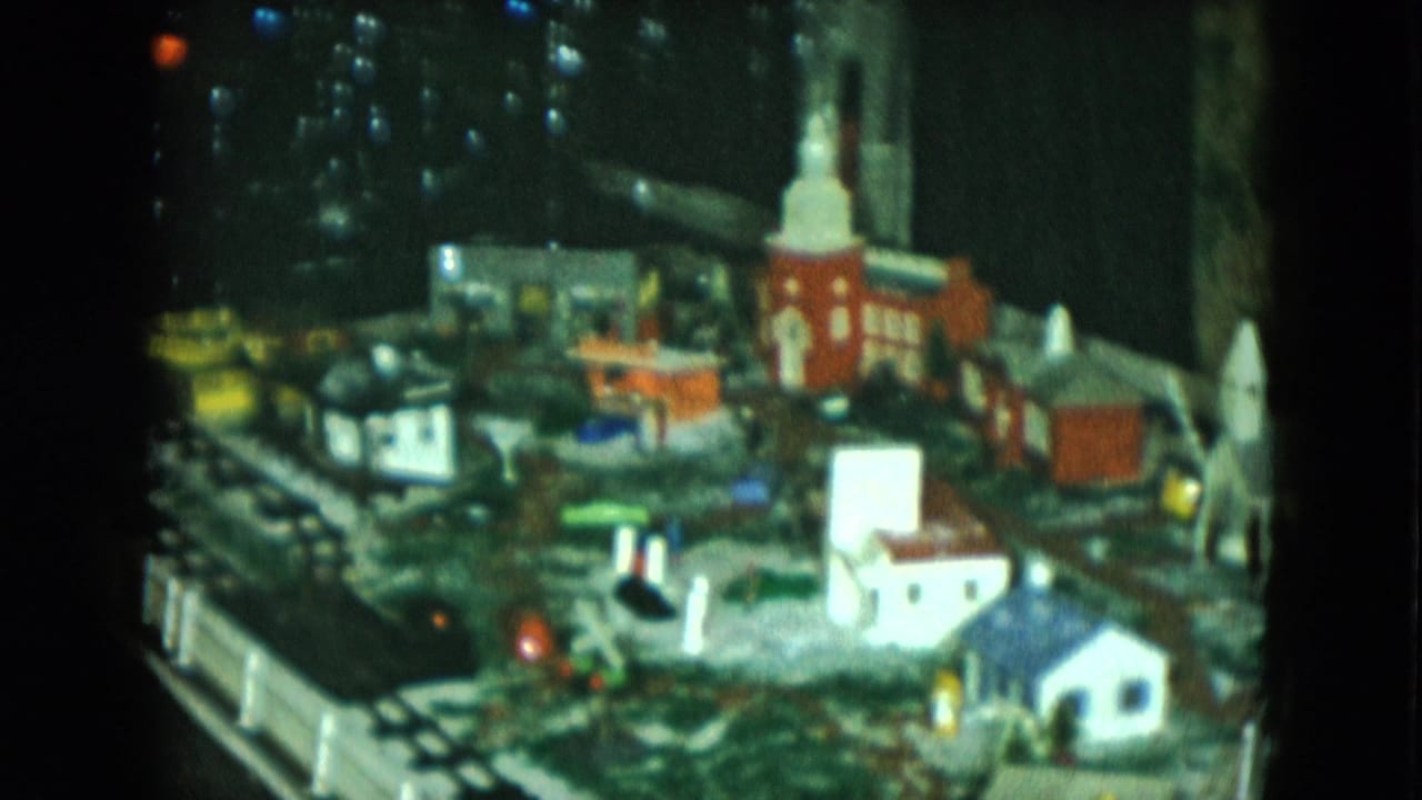 Miniature town scene with a red church, small houses, tracks, and lights.