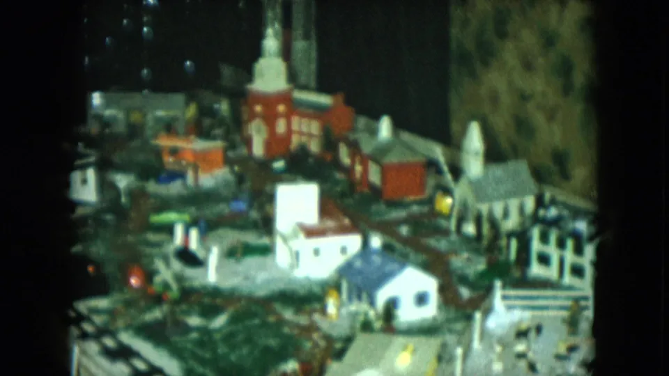 1951 Cleveland home-movie frame of a miniature railroad village with a red church, homes, track lines, and illuminated details.