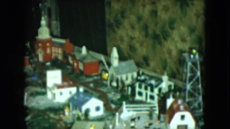 1951 Cleveland frame of the model town from later in the pan, with a church, homes, tracks, lights, and scenic background visible.