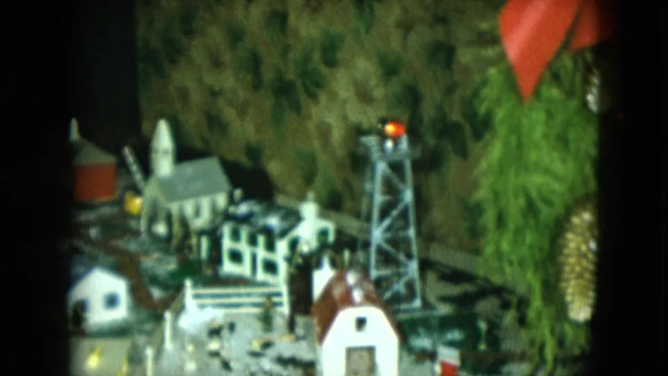 A Cleveland-area 1951 home-movie frame shows the model train display beside visible Christmas tree branches and a red tower light.