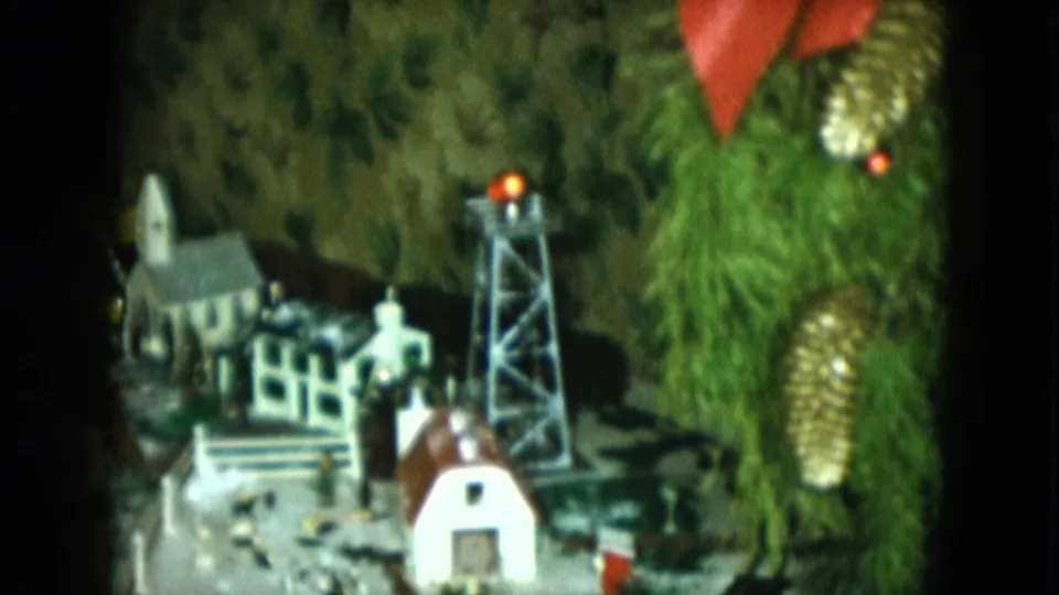 Final frame of the 1951 8mm model train scene, with the miniature town, track, tower, and Christmas tree branches in view.