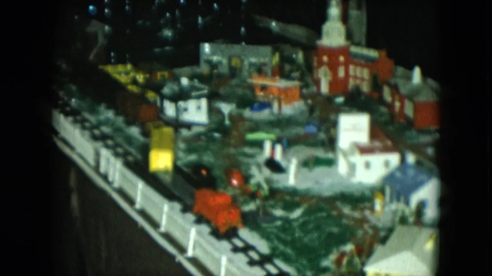 1951 Cleveland 8mm frame showing red and yellow model train cars beside a fenced miniature winter town display.