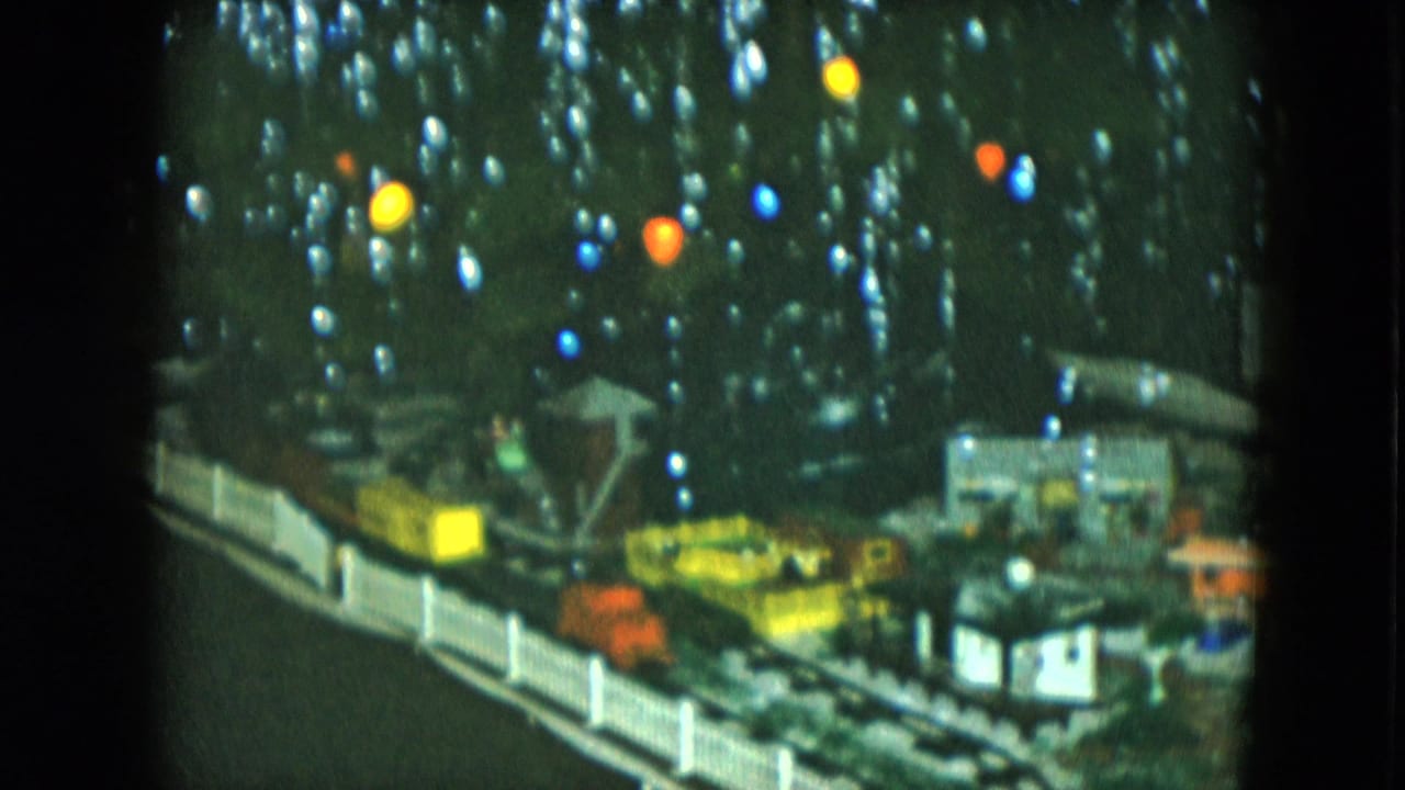 Miniature Christmas village and train tracks beneath colored tree lights.