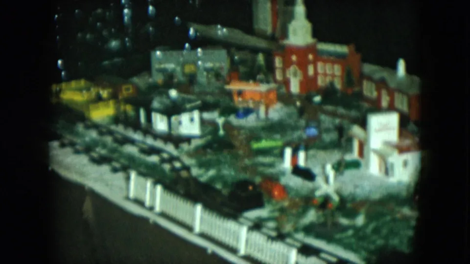 1951 Cleveland 8mm frame showing a black model locomotive moving through a miniature town display with buildings and fencing.