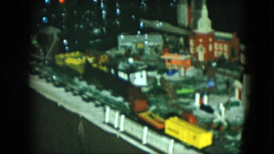 1951 Cleveland 8mm frame showing yellow and orange model train cars crossing a small illuminated town layout.