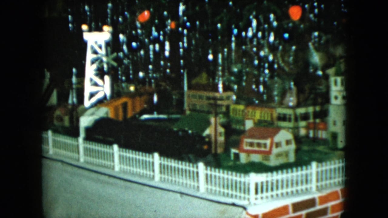 1951 Cleveland 8mm frame showing a tabletop toy railroad scene with small buildings, fencing, tinsel, and red ornaments.